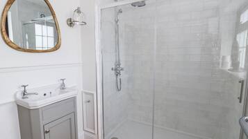 Un baño con ducha envuelta en vidrio, tocador con espejo y suelo de baldosas.
