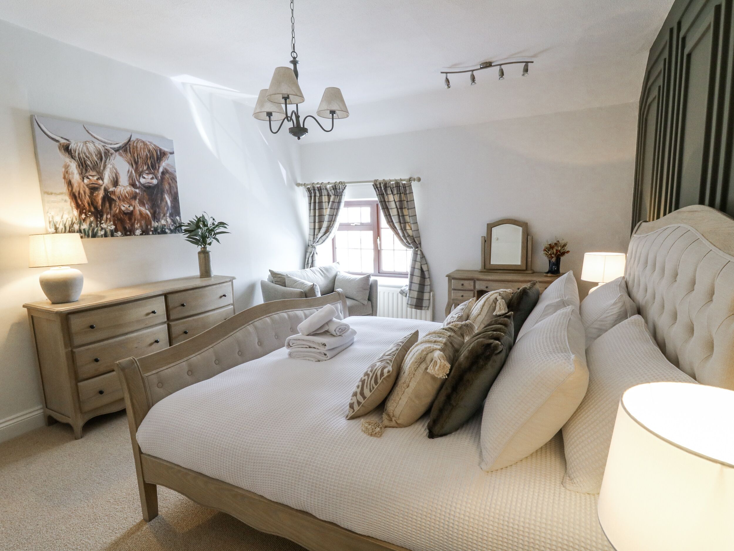 A bedroom with a bed, a dresser, a mirror, and a painting of animals.