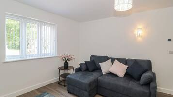 A modern living room with a grey sectional sofa, a small round table with a vase of flowers, a blue patterned rug, and a ceiling light fixture.