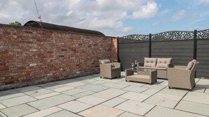 Une terrasse avec un mur en briques, une clôture en métal et du mobilier d’extérieur.
