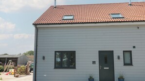 Un bâtiment à deux étages, doté d’un toit recouvert de tuiles rouges, d’une porte d’entrée et de deux fenêtres.