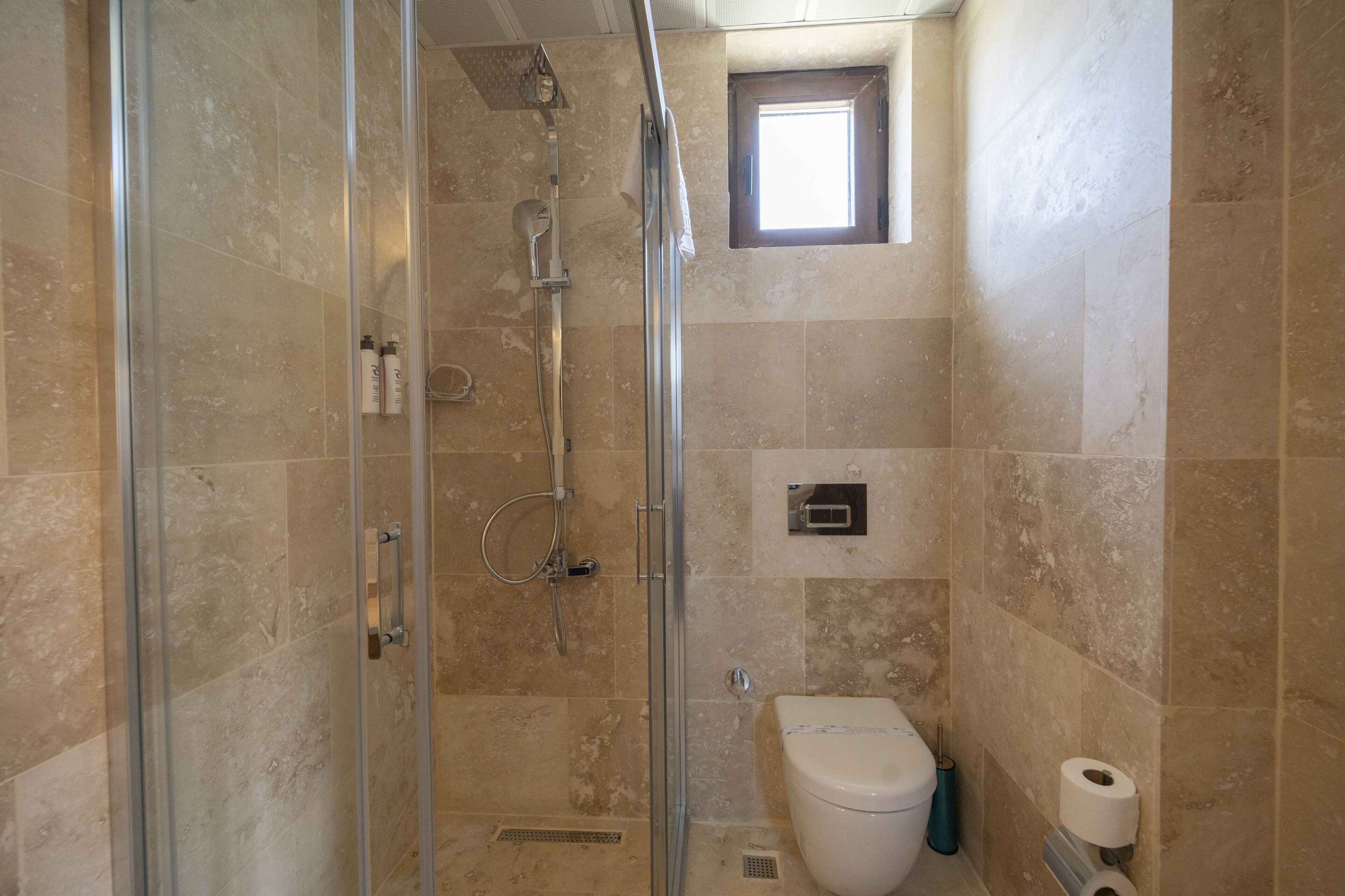 Un baño con cabina de ducha de vidrio, inodoro y una pequeña ventana.