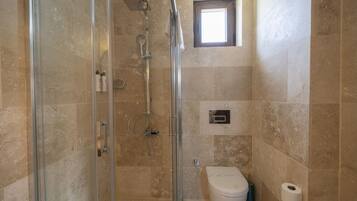 Un baño con cabina de ducha de vidrio, inodoro y una pequeña ventana.