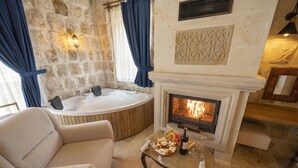 Una habitación acogedora con pared de piedra, chimenea, bañera y sofá.