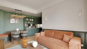 Un salon moderne avec un canapé, une table à manger et des chaises. On aperçoit un coin cuisine au fond.