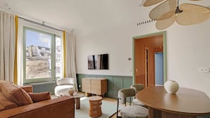 Une pièce bien éclairée, avec un canapé, des fauteuils, une table à manger et un téléviseur fixé au mur.