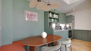 Un coin repas avec une table et des chaises en bois, un vase posé sur la table, et une cuisine en arrière-plan.