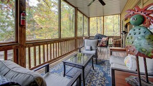 A covered porch with a glass table, wicker furniture, and a view of trees.