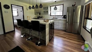 Een moderne keuken met een centraal eiland, barkrukken, roestvrijstalen apparatuur en hangende lampen.