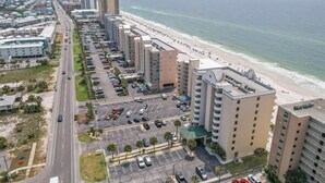 A coastal hotel with multiple floors, a parking lot, and a beach view.