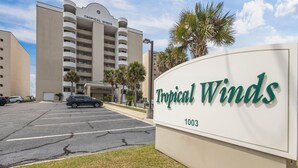 A sign for Tropical Winds hotel with a parking lot in front.