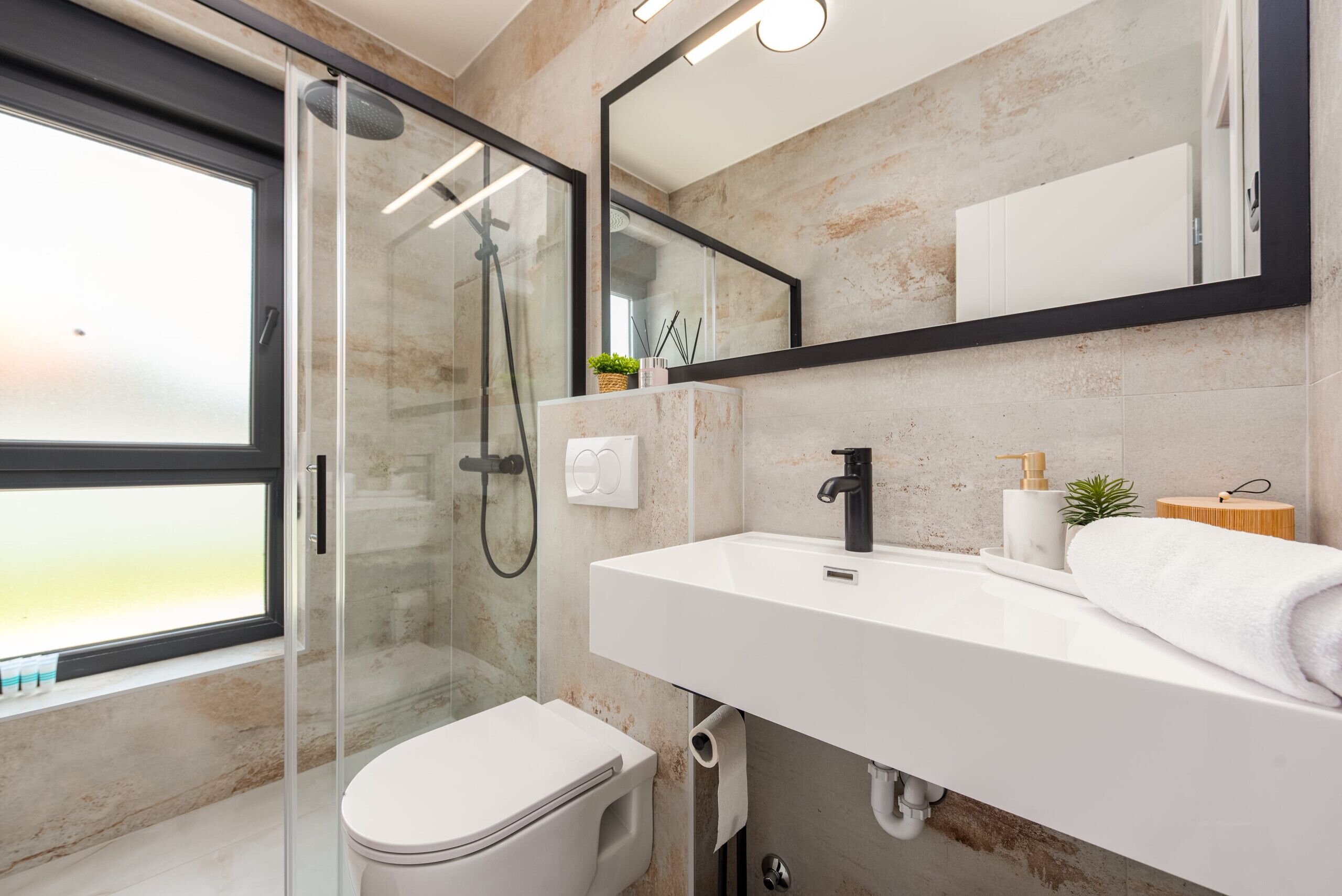 A modern bathroom with a glass shower enclosure, a white sink, and a large mirror.