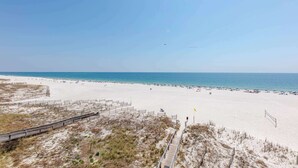 Une plage avec une promenade en bois menant au rivage, une plage de sable et un ciel bleu dégagé.
