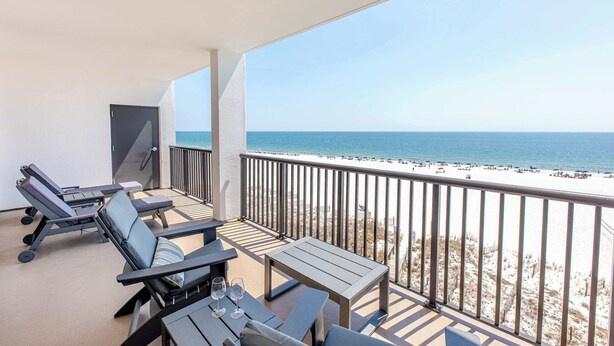 Un balcon avec des fauteuils et une table, donnant sur une plage.