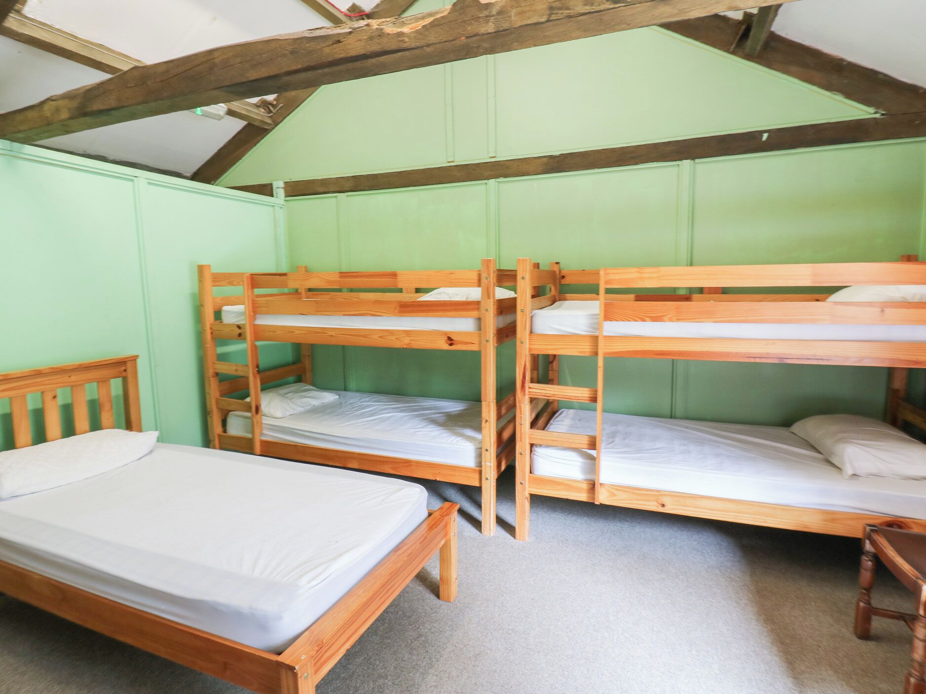 Une chambre avec des lits superposés, un lit simple et une chaise en bois.