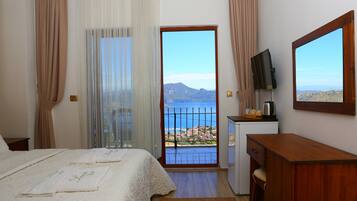 Habitación de hotel con cama, escritorio, televisión y balcón con vistas al mar y a las montañas.