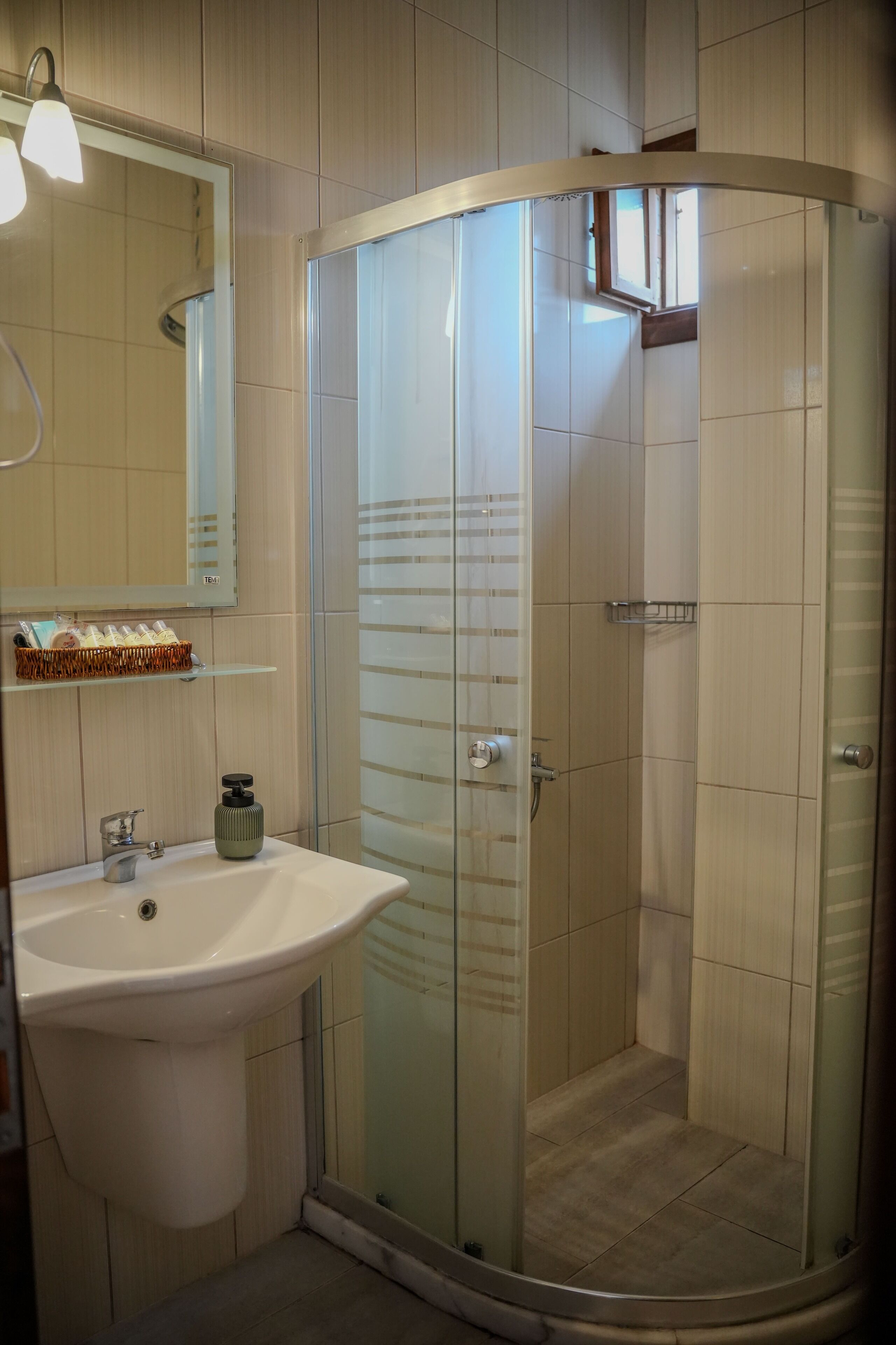 A modern bathroom with a glass-enclosed shower, a sink with a soap dispenser, and a mirror above the sink.