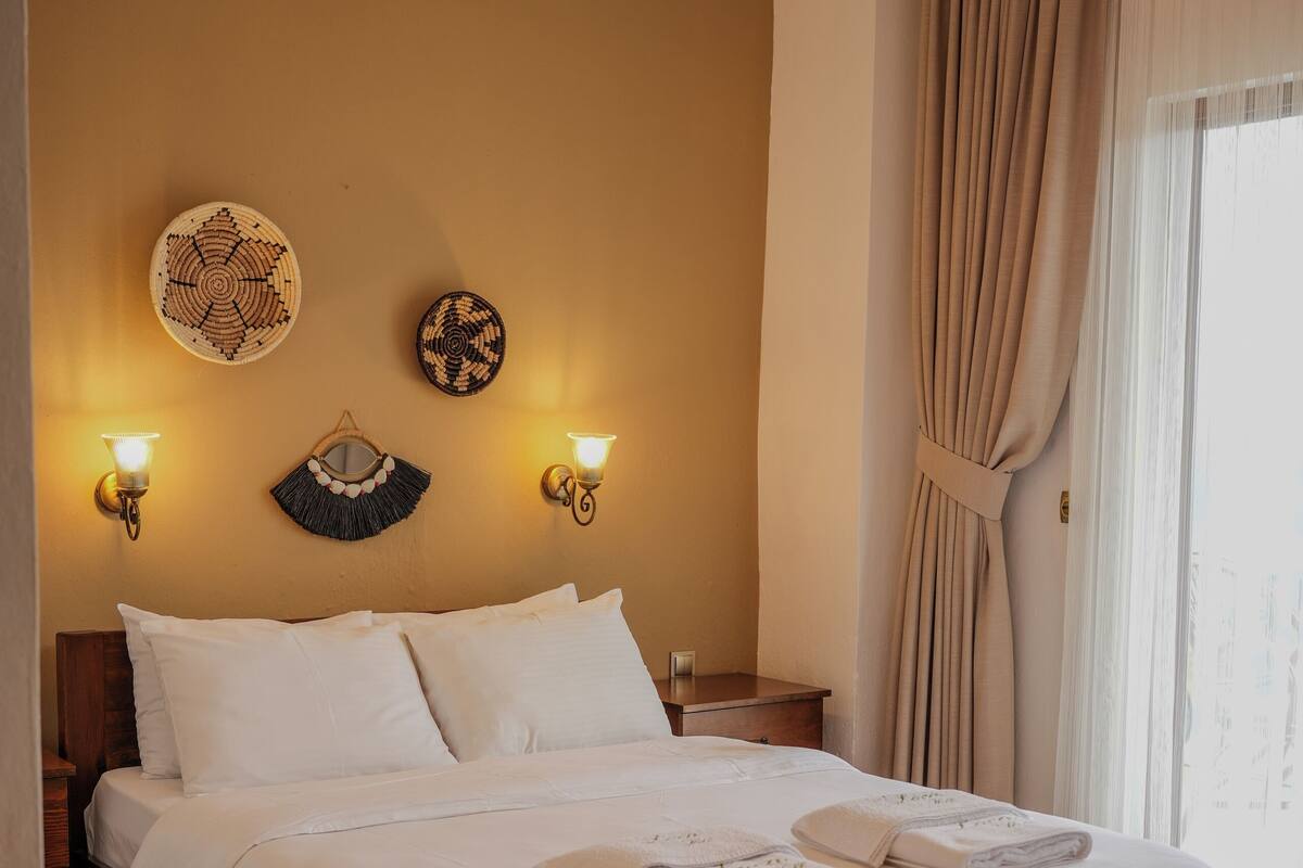 A neatly made bed with white linens, a wooden headboard, and a wall-mounted air conditioner.