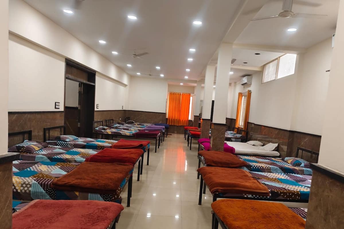 Habitación de hotel con varias camas dispuestas en filas, un ventilador de techo y un ventanal con cortinas naranjas.