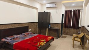 A hotel room with a bed, a desk, a wardrobe, an air conditioning unit, and a curtain. - Agrawal Bhawan (Ujjain)