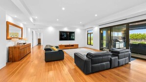 Un salon moderne avec un plancher en bois, un grand téléviseur à écran plat, un ensemble de canapés et une porte-fenêtre coulissante donnant sur un espace extérieur.