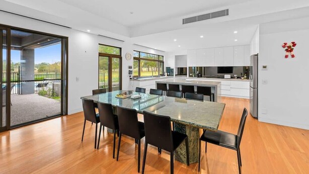 Une cuisine moderne avec des meubles blancs, un grand îlot central et un coin repas comprenant une table et des chaises en verre.