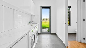 Une cuisine moderne équipée d’un lave-linge et d’un sèche-linge intégrés, d’une grande fenêtre et offrant une vue sur un champ verdoyant.