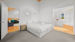 A bedroom with a large bed, a wooden ceiling, and a bathroom with a sink and mirror.