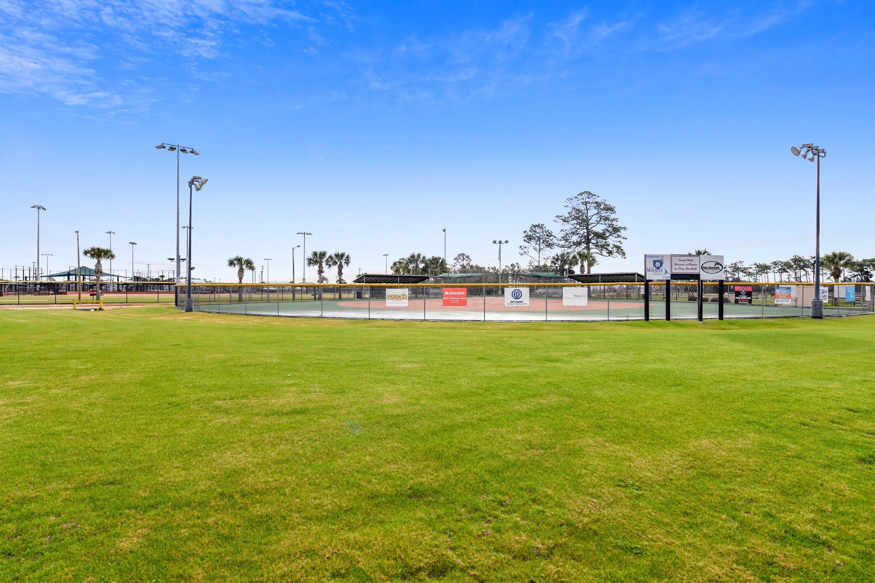 A baseball field with a fence, floodlights, and a scoreboard.