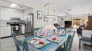 Una cocina moderna con armarios blancos, electrodomésticos de acero inoxidable y una zona de comedor con una mesa dispuesta para cuatro personas.