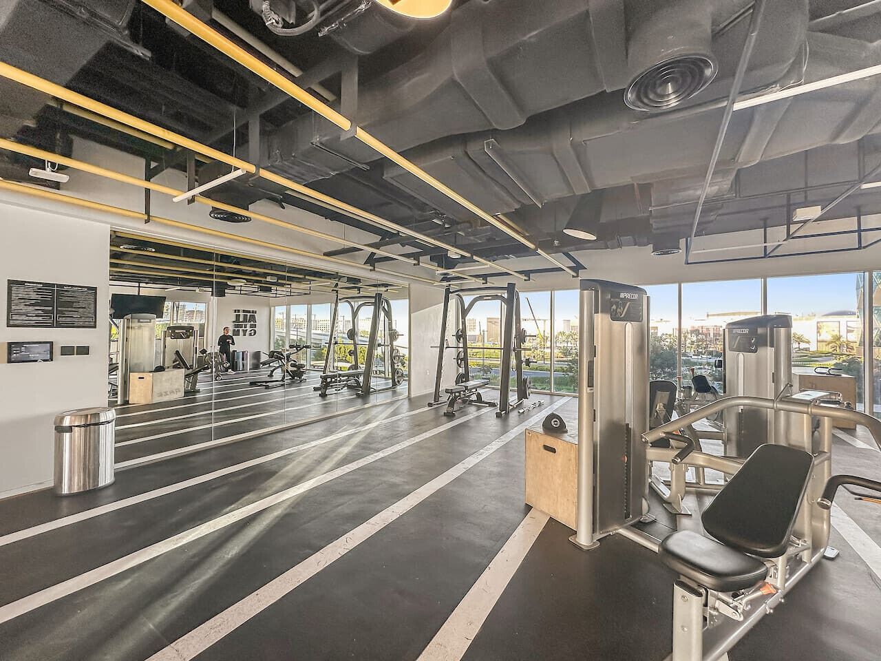 A modern gym with various exercise equipment, large windows, and a clean, industrial design.