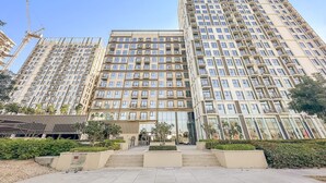 Un immeuble résidentiel de grande hauteur, doté de nombreux balcons, d’une entrée principale et d’une cour aménagée.