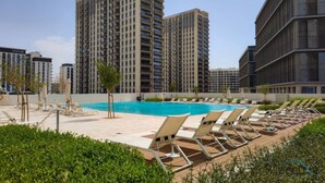 Un hôtel doté d’une piscine, de chaises longues et dont l’arrière-plan est constitué d’immeubles de grande hauteur.