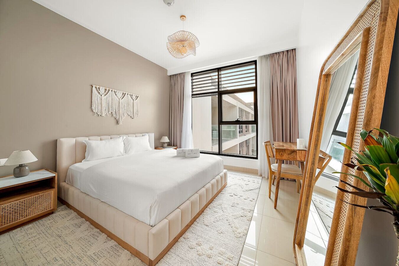 A bedroom with a bed, bedside tables, a desk, a chair, a large mirror, and a window with blinds.