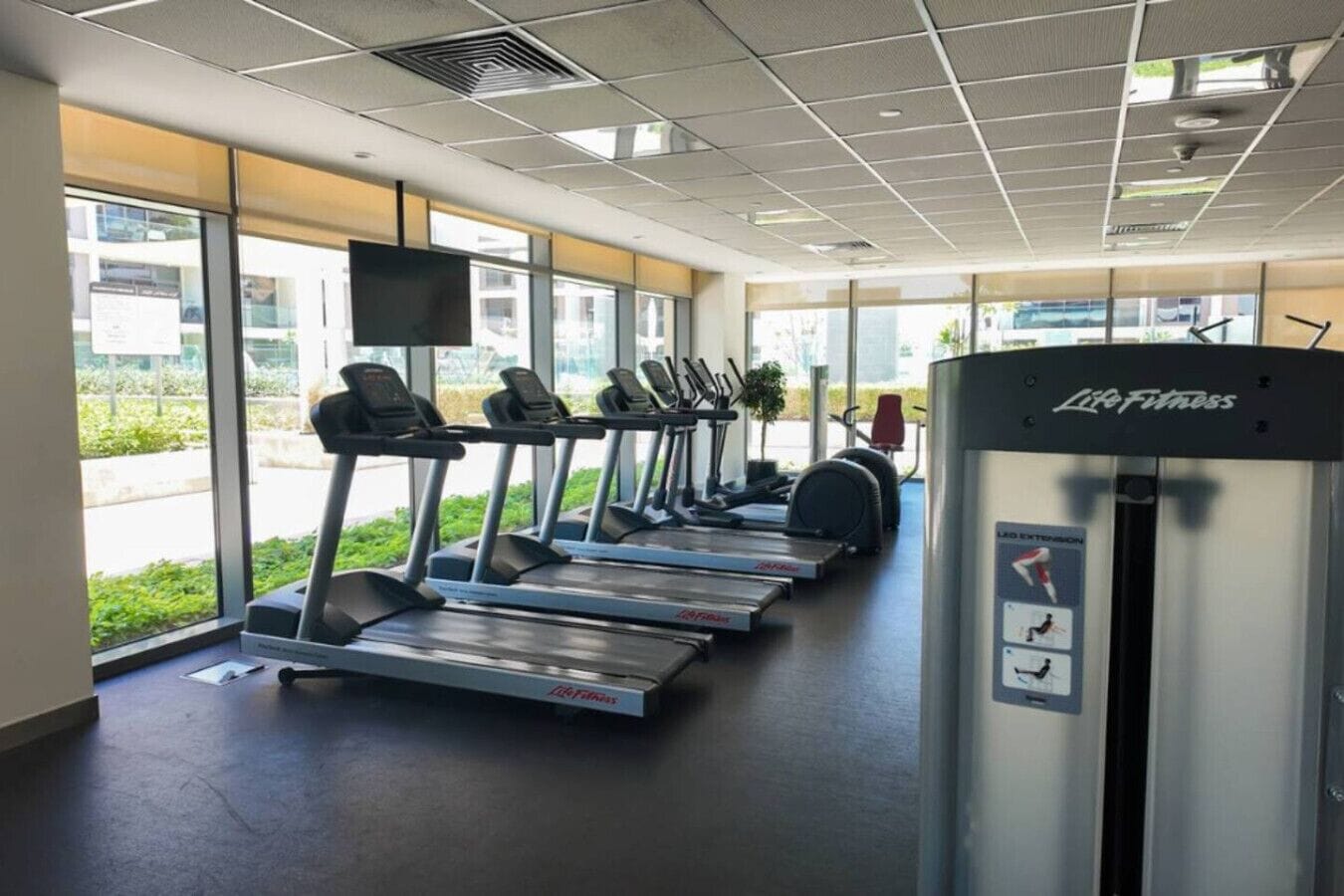 A gym with treadmills, a Life Fitness machine, and large windows.