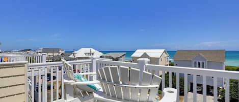 A balcony with white railings overlooking a beach with houses in the background.