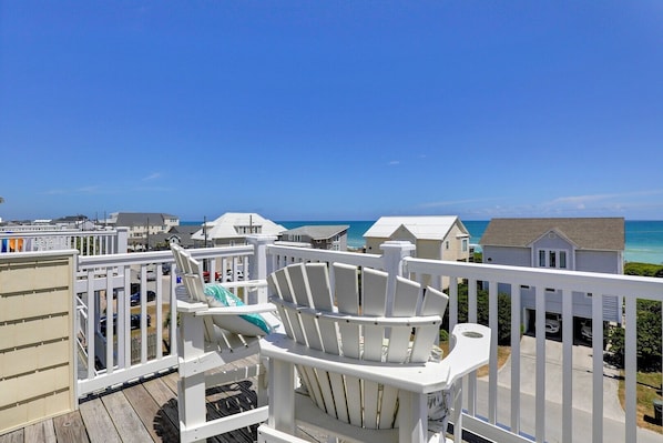 A balcony with white railings overlooking a beach with houses in the background.