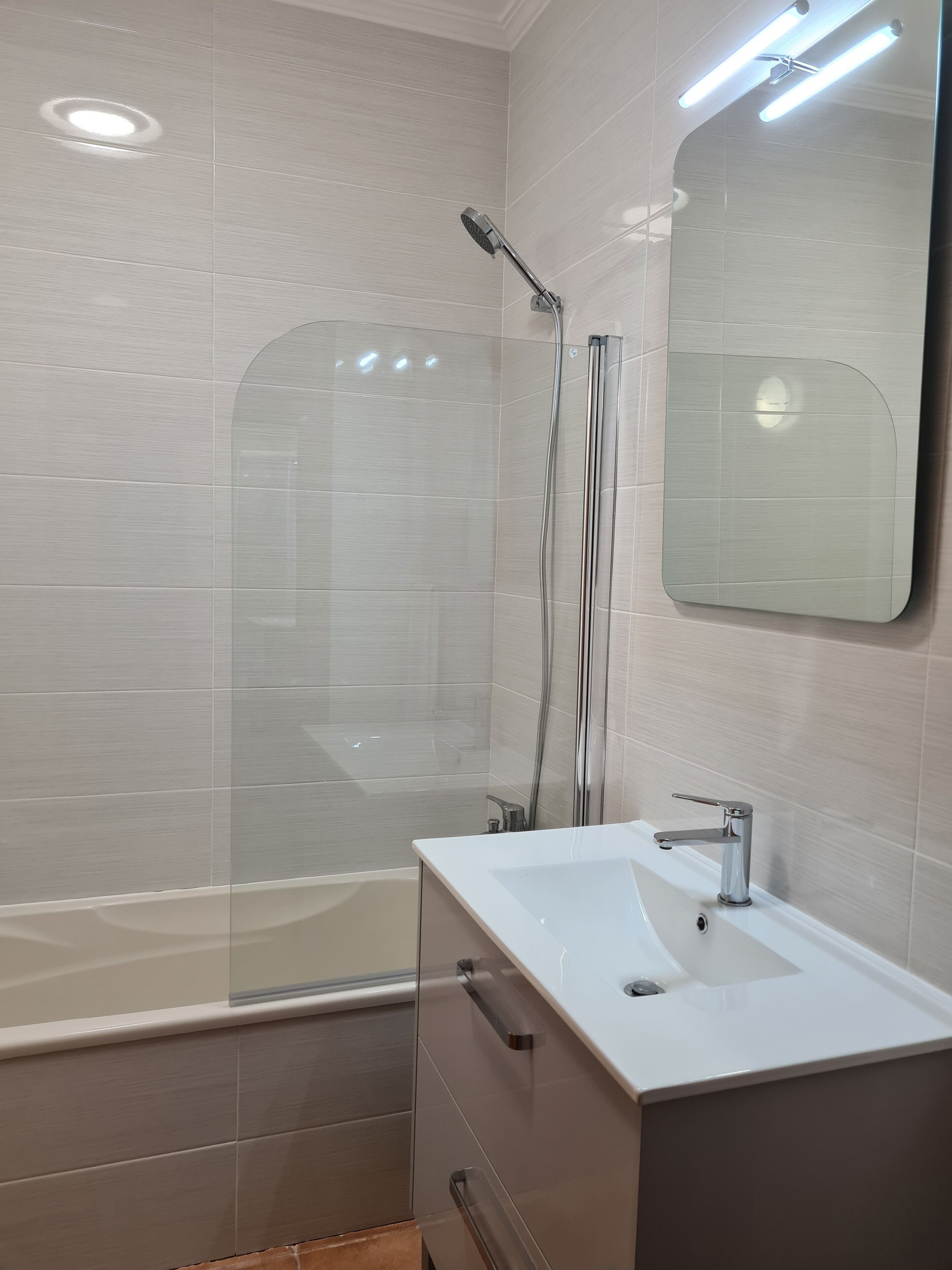 Ein modernes Badezimmer mit Duschkabine aus Glas, einem weißen Waschbecken und einem großen Spiegel.