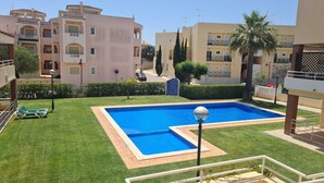 En swimmingpool omgiven av välskött gräsmatta, med utsikt över bostadshus i bakgrunden.