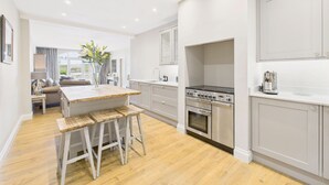 A modern kitchen with a central island, stainless steel appliances, and a view to the living area. - Host Stay Glenridge House Retreat (Wooler)