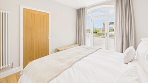 A bedroom with a large bed, a wooden door, a bench, and a view of the outdoors. - Host Stay Glenridge House Retreat (Wooler)