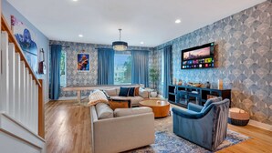 A modern living room with a sofa, armchairs, a coffee table, and a TV mounted on the wall. - Rooftop Deck Shuffleboard BBQ Near Downtown (Nashville)