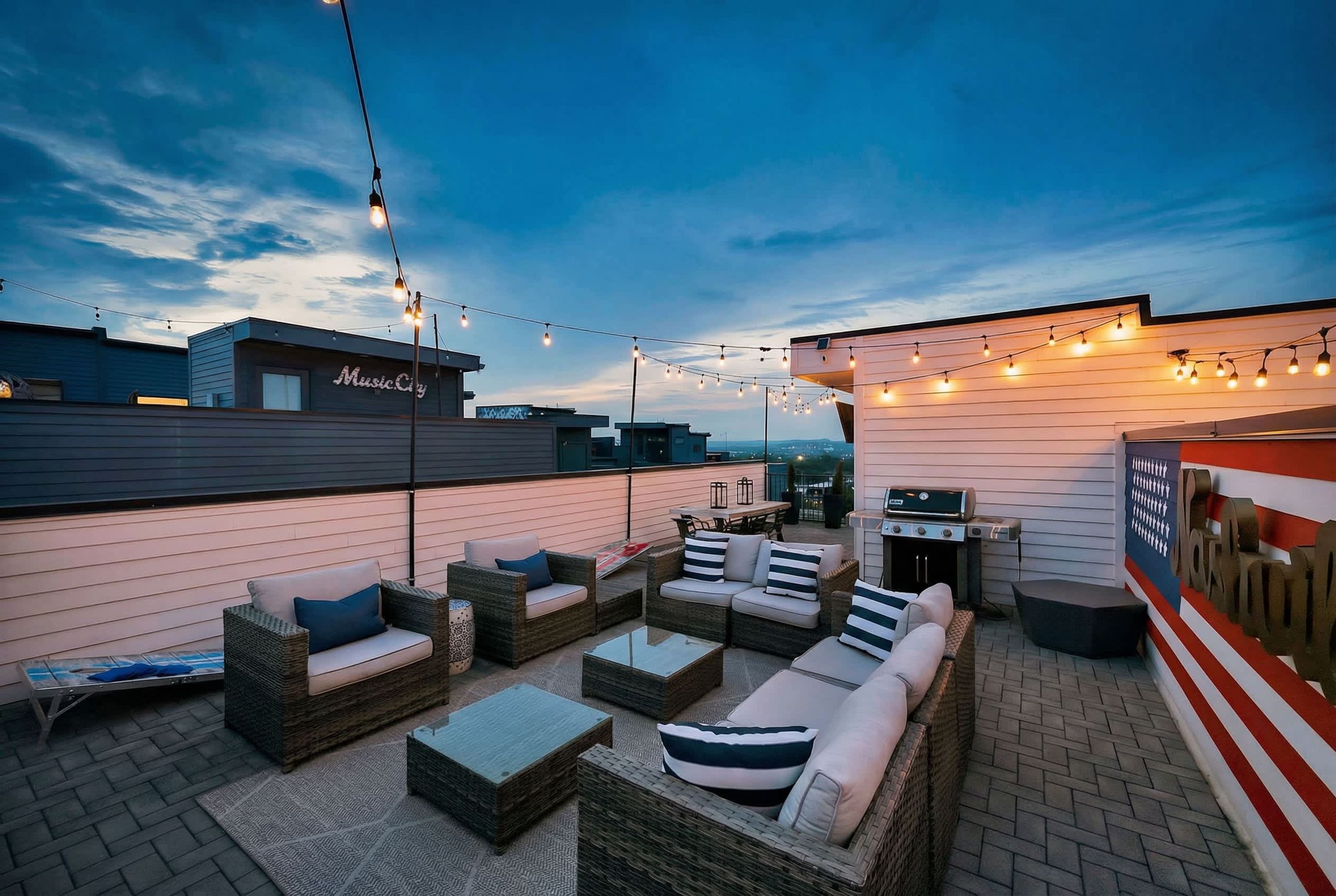 An outdoor patio area with wicker furniture, string lights, and a grill.