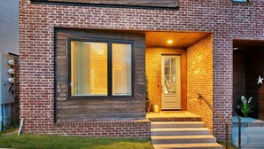A modern brick house with a wooden front door, a large window with blinds, and a small porch with steps. - Rooftop Deck Shuffleboard BBQ Near Downtown (Nashville)