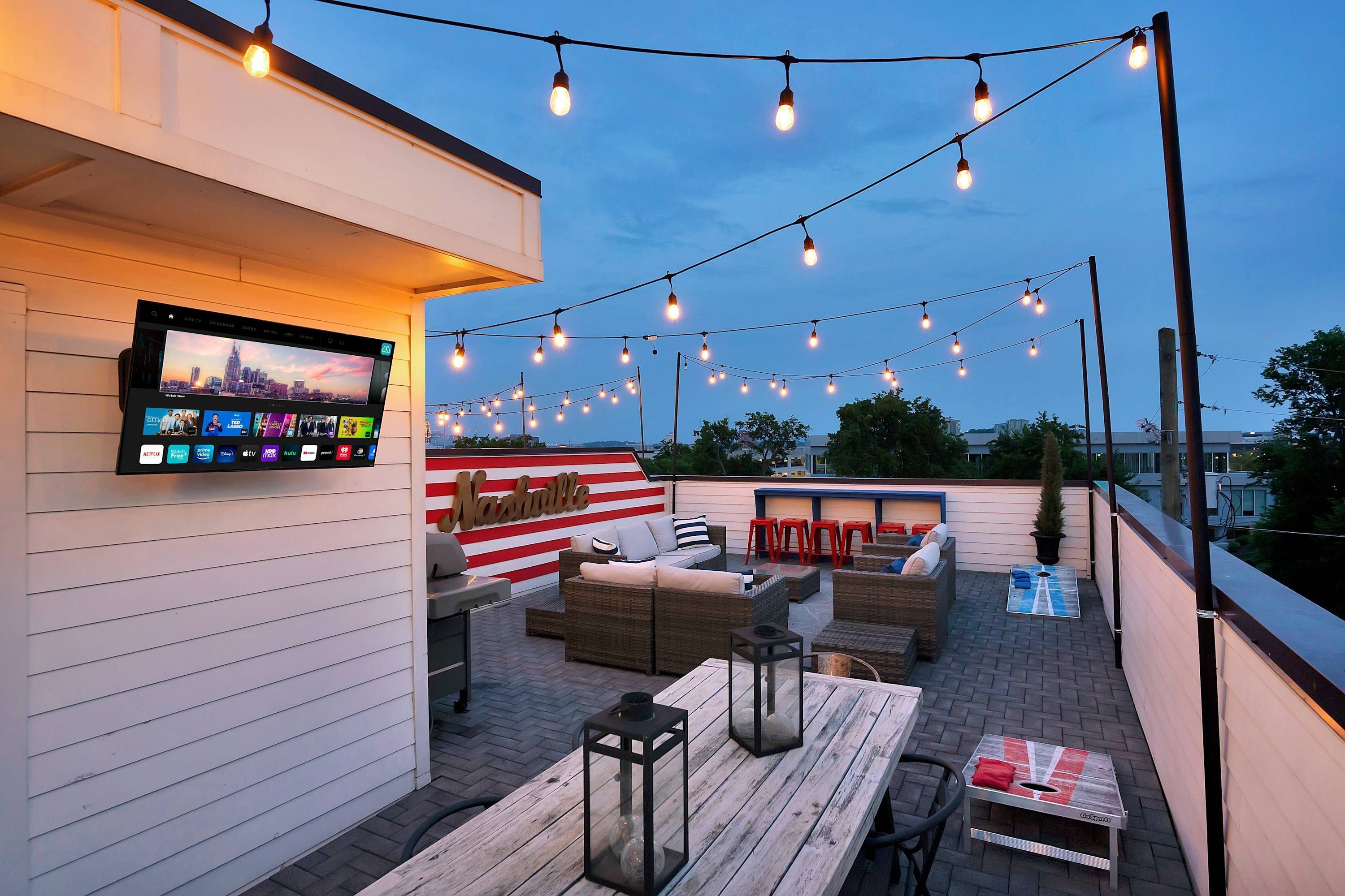 Une terrasse sur le toit, décorée de guirlandes lumineuses, avec un téléviseur à écran plat, du mobilier d’extérieur et un panneau indiquant « Nashville ».