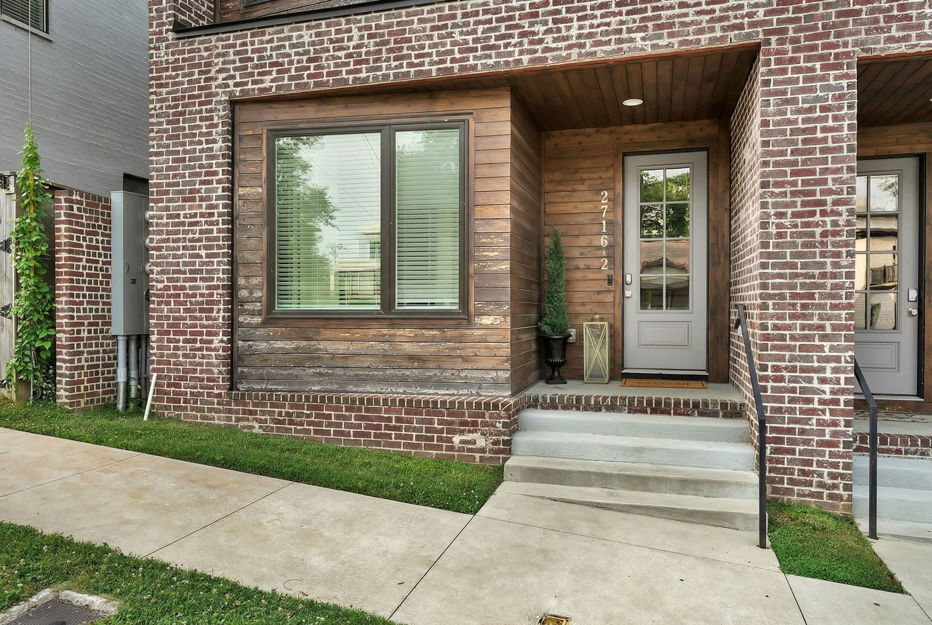 A modern brick house with a large window, a front door, and a small porch.