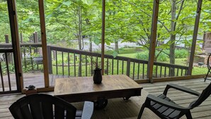 A wooden deck with a table and two chairs, overlooking a lush garden and a body of water.