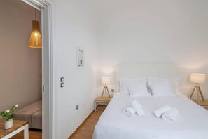A hotel room with a large bed, two bedside tables with lamps, a small table with a plant, and a door leading to another room. - Athens Cozy Residence Near Acropolis (Athens)