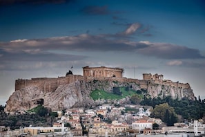 A historic cityscape with ancient ruins on a hill, modern buildings below, and a clear sky.