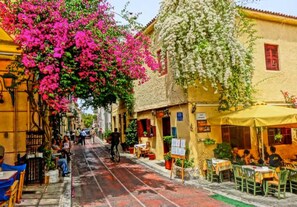 A narrow street lined with yellow buildings, outdoor seating, and greenery. - Athens Residence - Cozy Gem Near Acropolis (Athens)